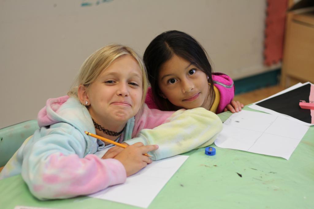 Two students seated at an art table with pencils and paper, posing for the camera