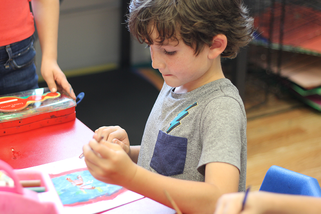 Student seated at a table works on a watercolor painting