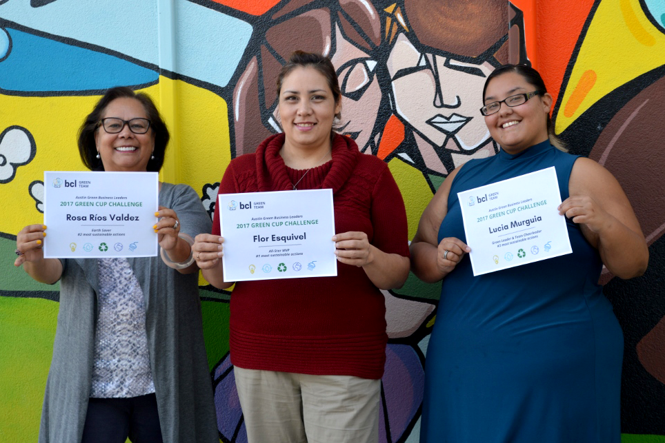 Rosa and two other BCL employees showing off their Green Cup certificates. Colorful mural in background.