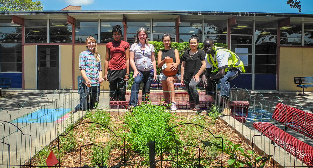 Eastside memorial students with City staff pose behind a garden on campus.