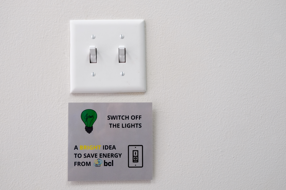 Light switch with sign saying "Switch off the lights. A bright idea to save energy from BCL"