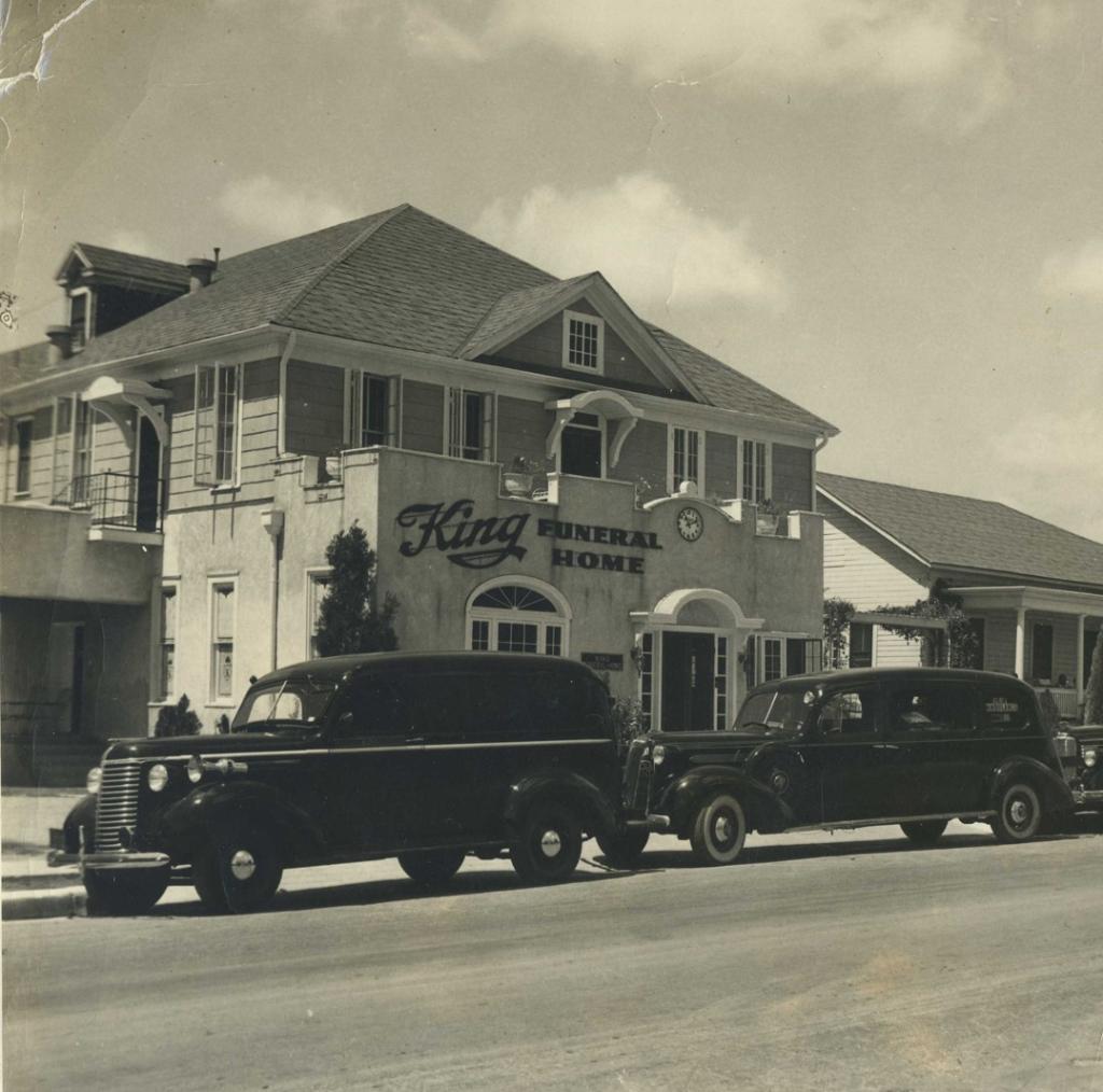 Black and white picture of King Funeral Home with black cars parked on street