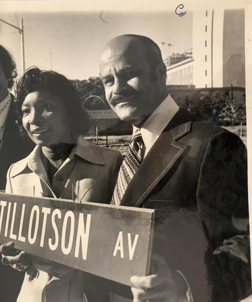 Black and White of JQTKing standing beside woman and holding Huston-Tillotson Ave sign