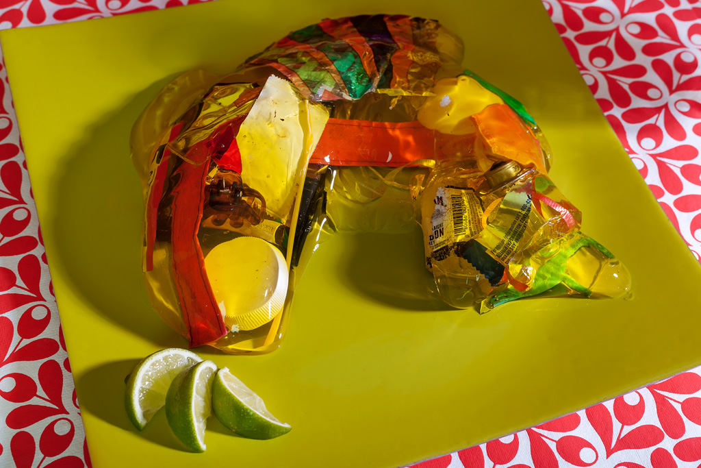 A photograph of a jello fish filled with trash on a carefully serving plate with slices of limes next to it