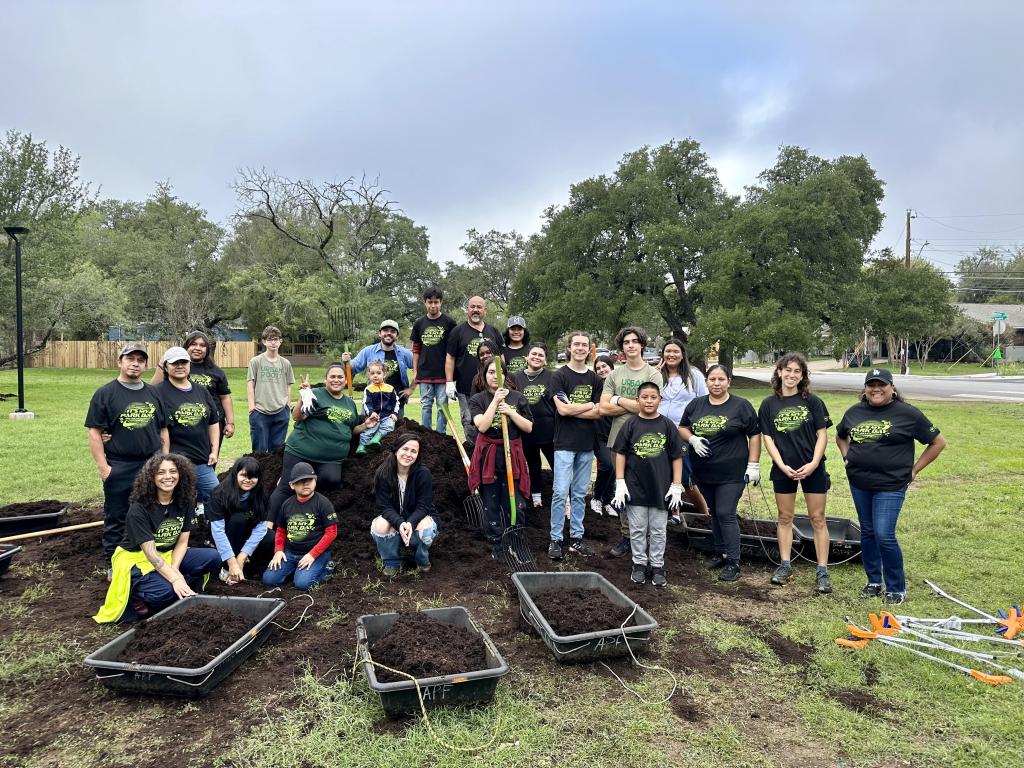 A group of 25 volunteers poses in a park with mulch sleds