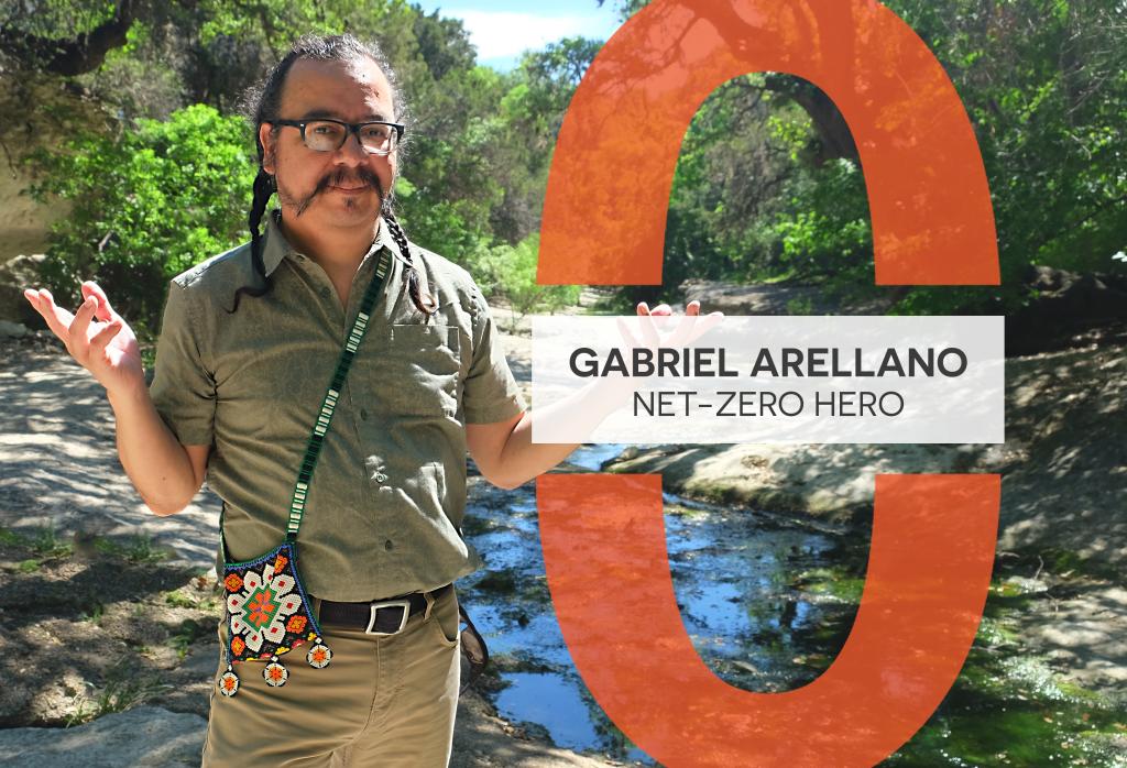 Gabriel Arellano stands in front of Blunn Creek. He is wearing dark glasses and has shoulder-length black hair in two braids. He is wearing a neutral outfit with a small, colorful, beaded bag worn across his body.