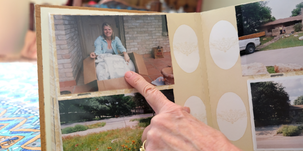 A close up of a finger pointing out a photo in an album. The photo shows a younger Susan sitting on her porch with a giant cardboard box full of seeds.