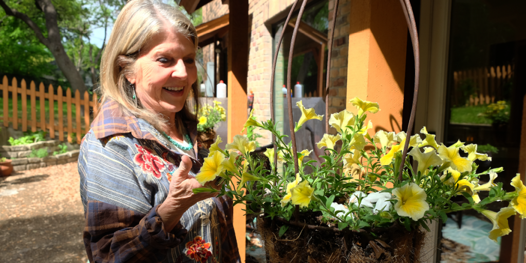 Susan stands next to a hanging basket filled with yellow petunias.
