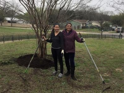 Photo: Two woman smile at the camera in front of a tree with mulch