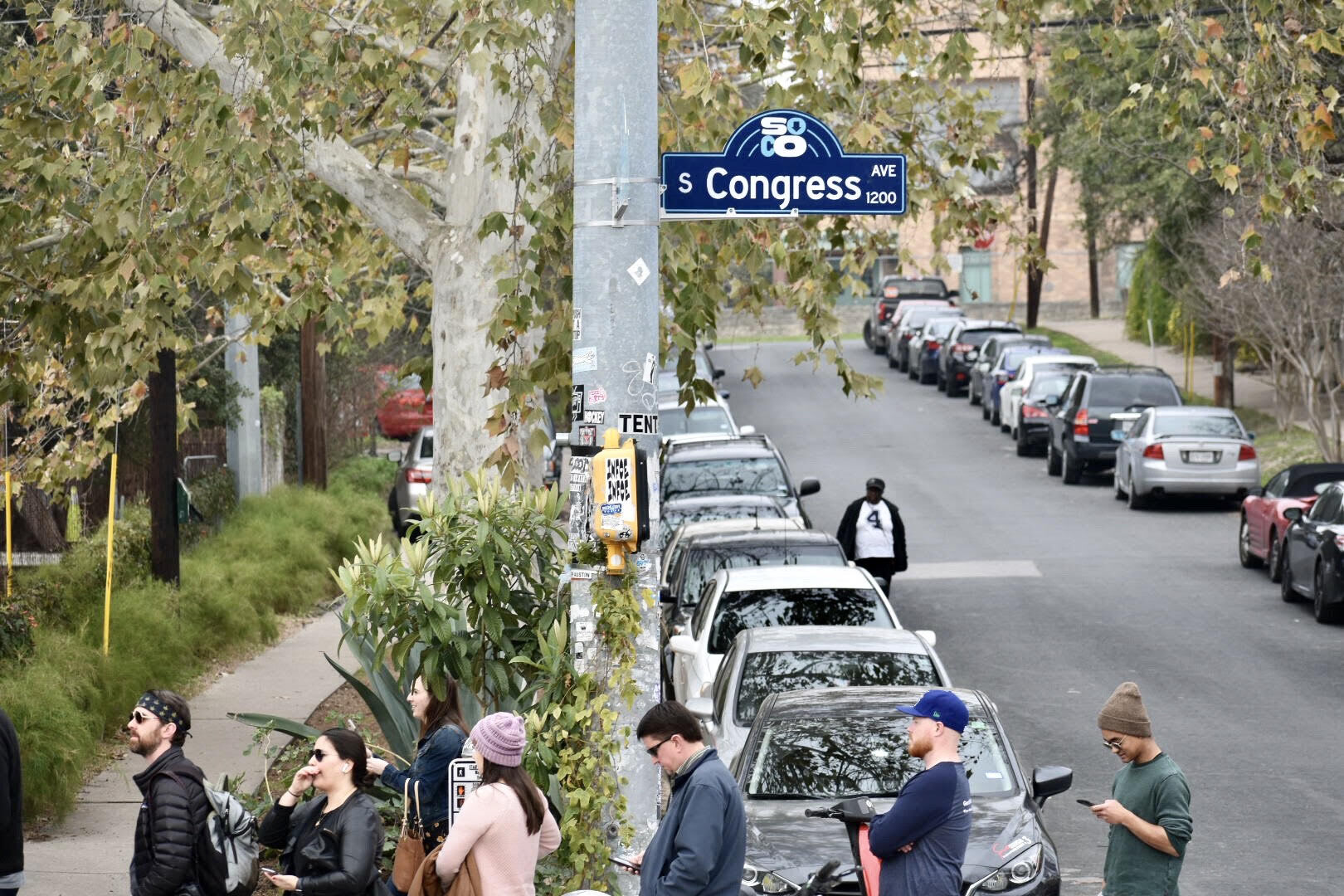 People crossing a local Austin neighborhood street filled with parked vehicles