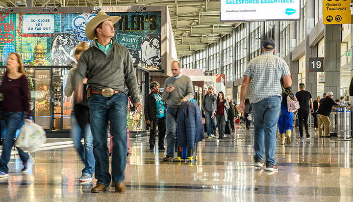 Man dressed in western wear and cowboy hat walking in a busy airport terminal.
