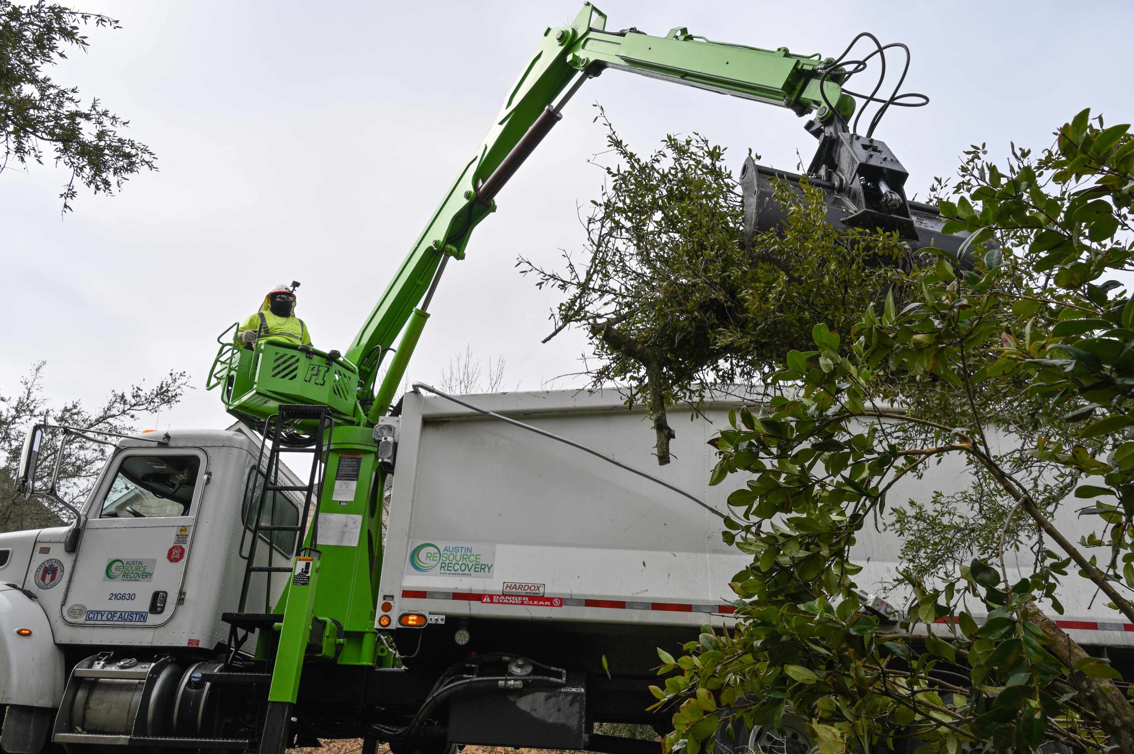 An Austin Resource Recovery employee operates a crane to collect a large brush pile from a residential customer.