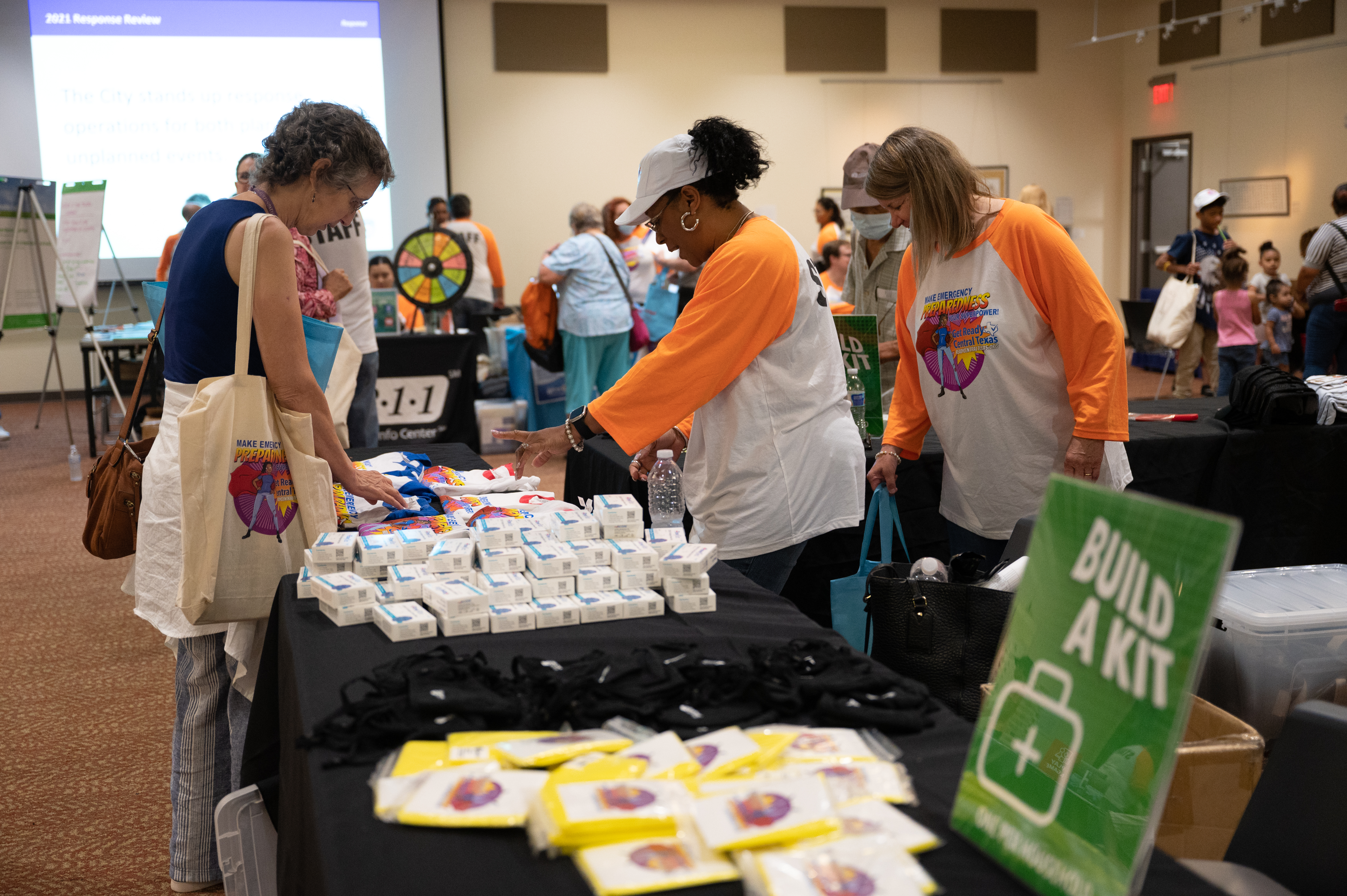 Image of 3 women at a table with various emergency kit materials. Sign in foreground reads, "Build a kit!"