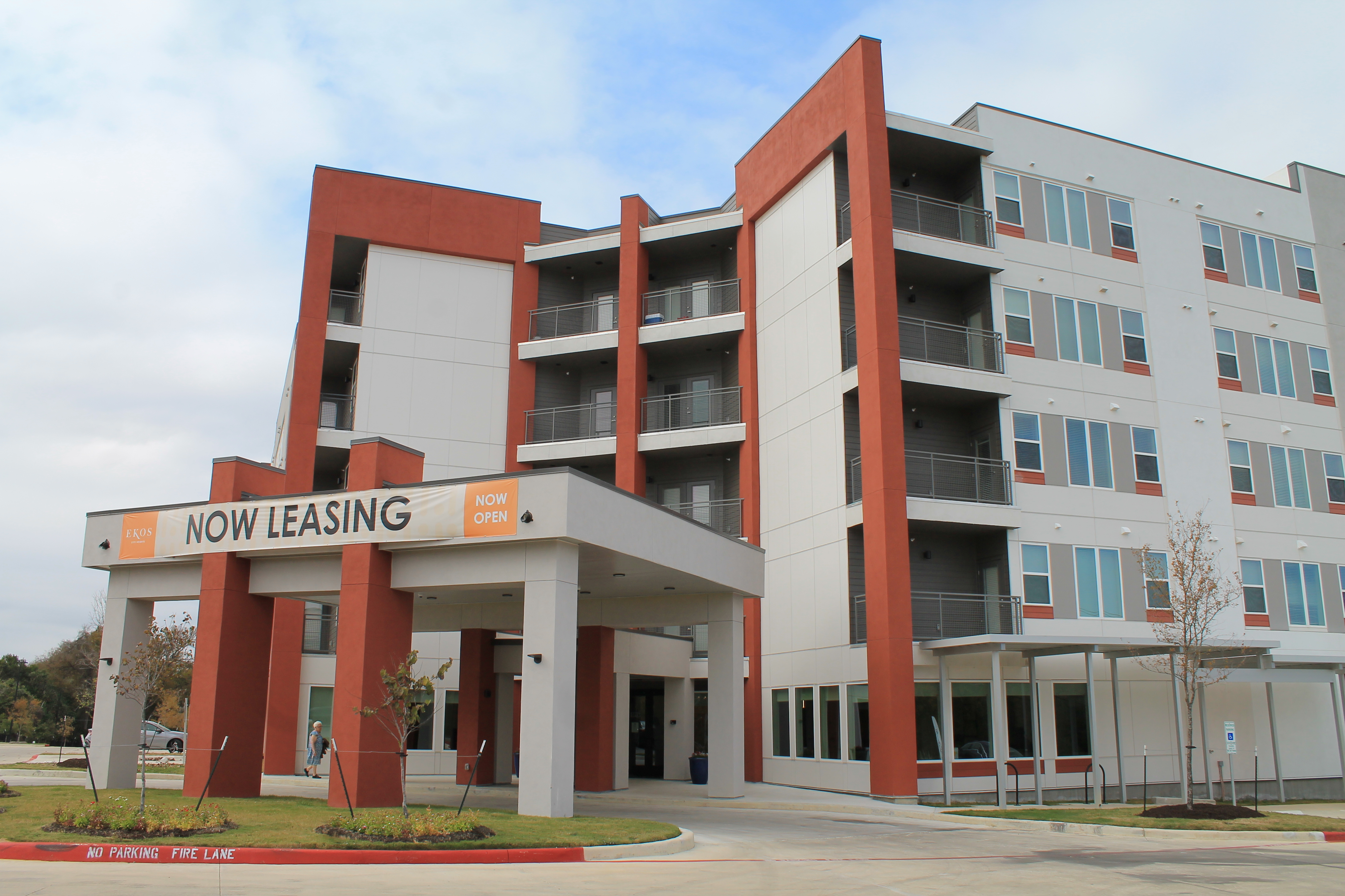 Rendering shows a multi-story white building with a red columns and red corners at the entrance. The building also has a covered entrance that is large enough for vehicles to pass under.