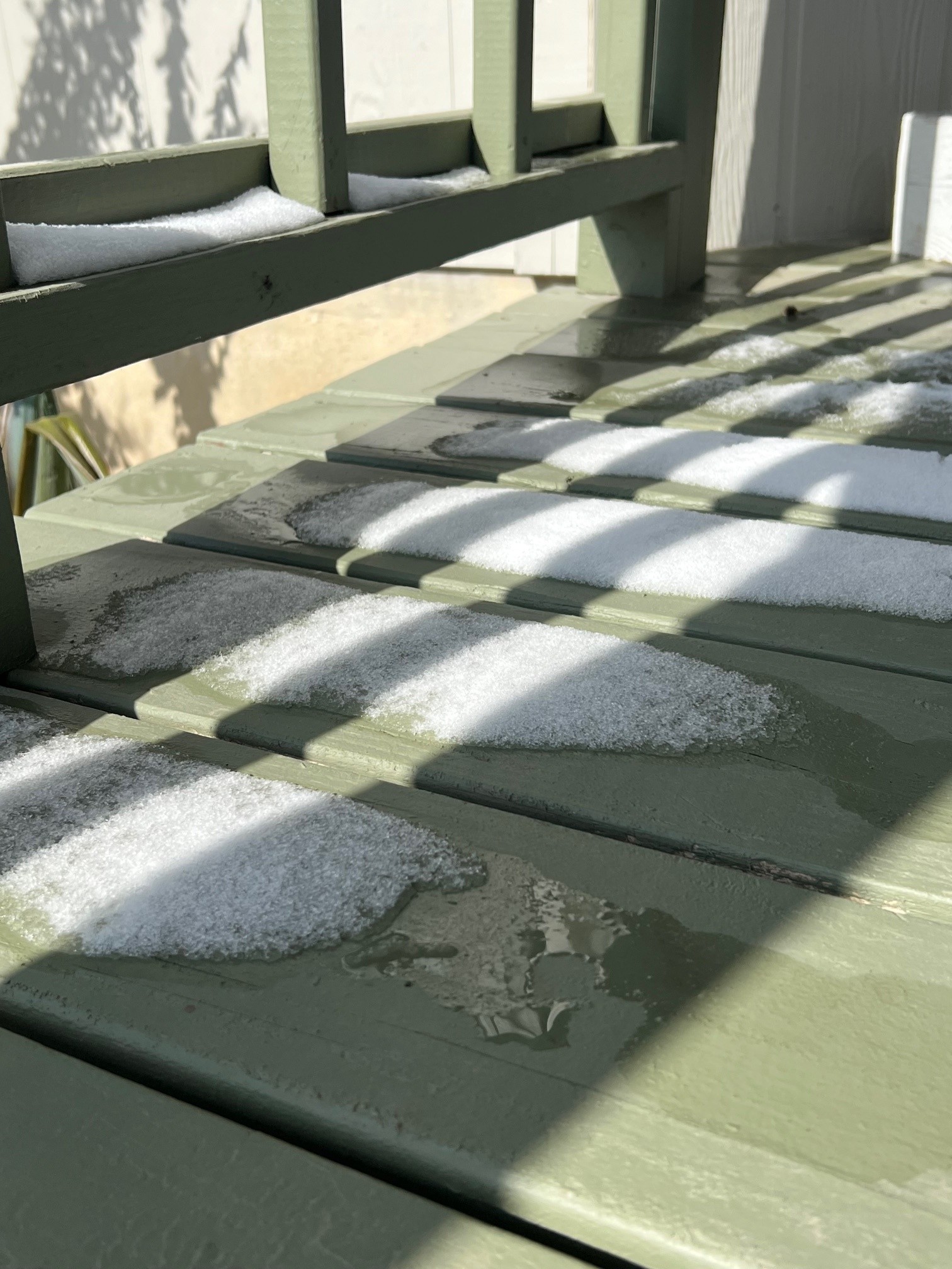 Snow in the sunshine melting on a green wooden deck