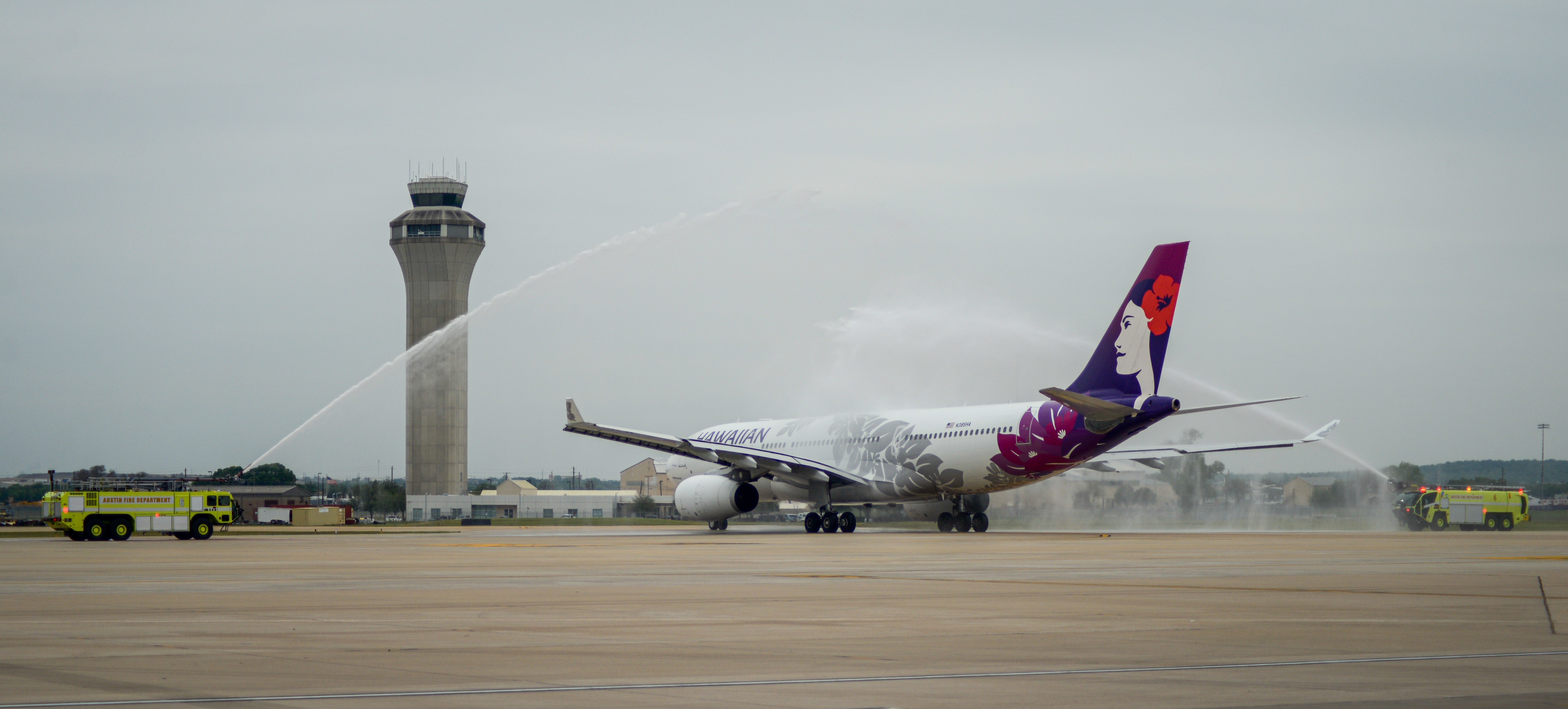 photo of a Hawaiian Airlines Airbus A330 taxiing to the runway as it receives a water canon salute.