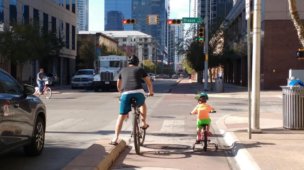 A person and a child riding bikes side by side at a red light on a city street
