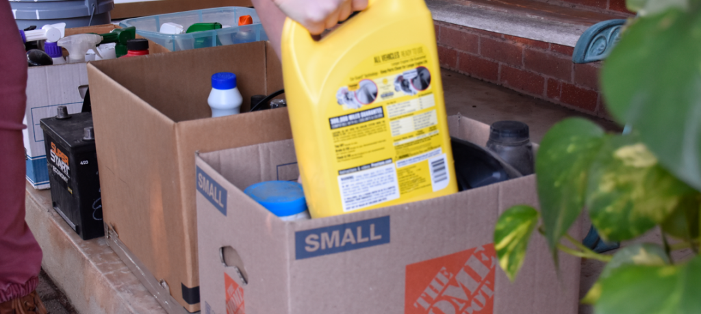 HHW materials such as cleaning supplies are loaded into a cardboard box.