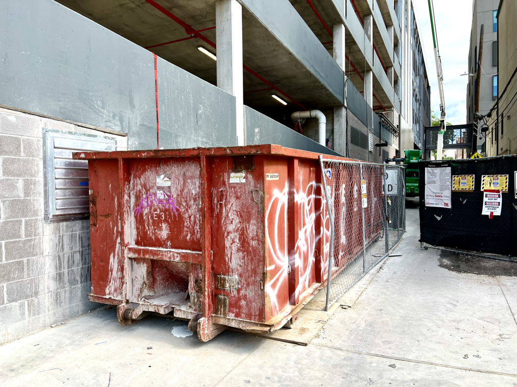 A multifamily building being constructed with a large brown trash cart in front. 