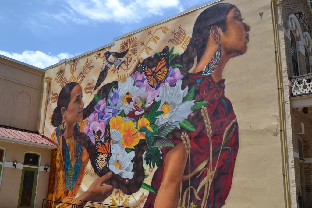 photo of mural on the side of the Old Bakery - mural depicts two women with braids, flowers, butterflies, and birds