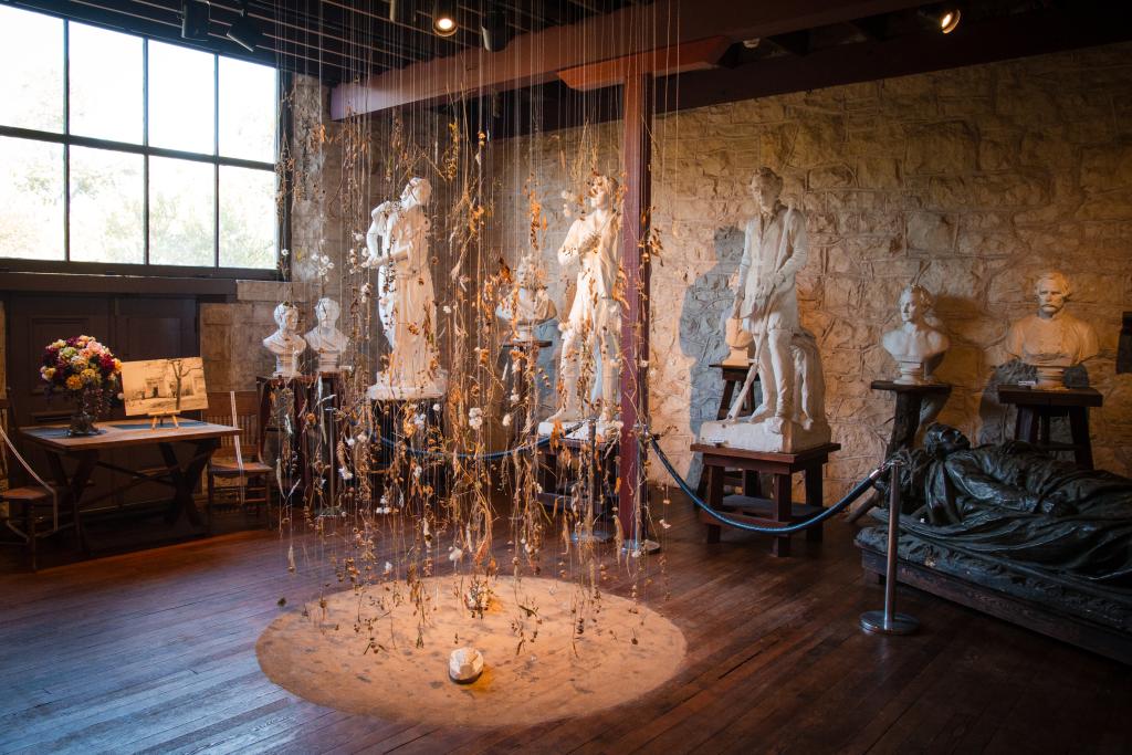 gallery full of sculptures with raining leaves art in the center