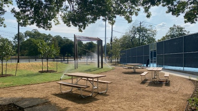 Photo of completed Pharr Tennis renovations, including picnic tables, resurfaced courts, landscaping, and an art installation. 