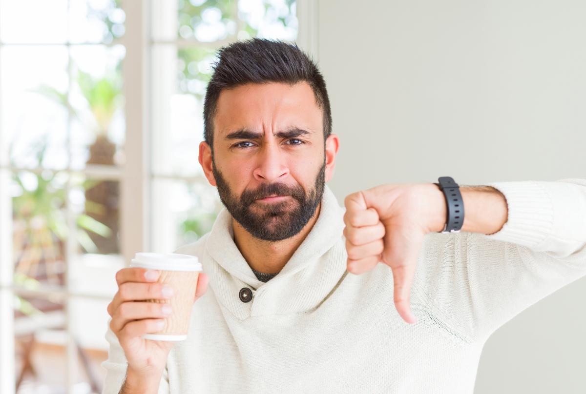 Man holding a single-use coffee cup and giving "thumbs down"