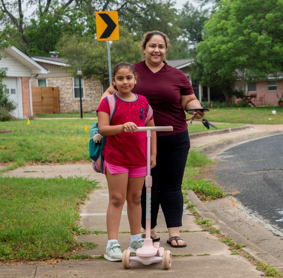 Girl and woman stand on sidewalk.