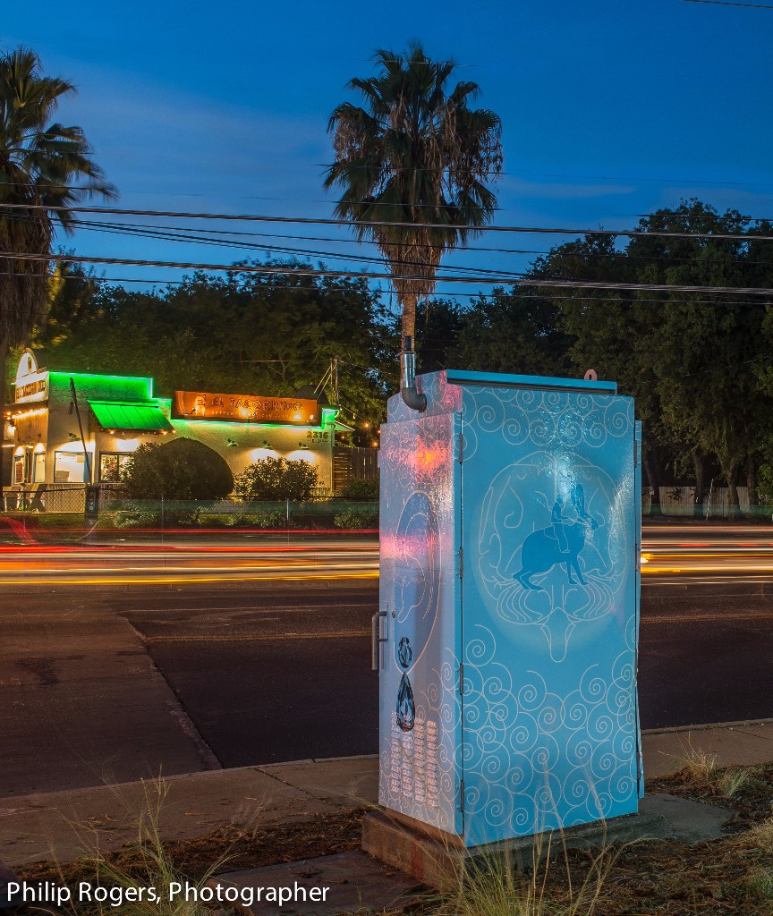 View of a colorful art box near a sidewalk at night.