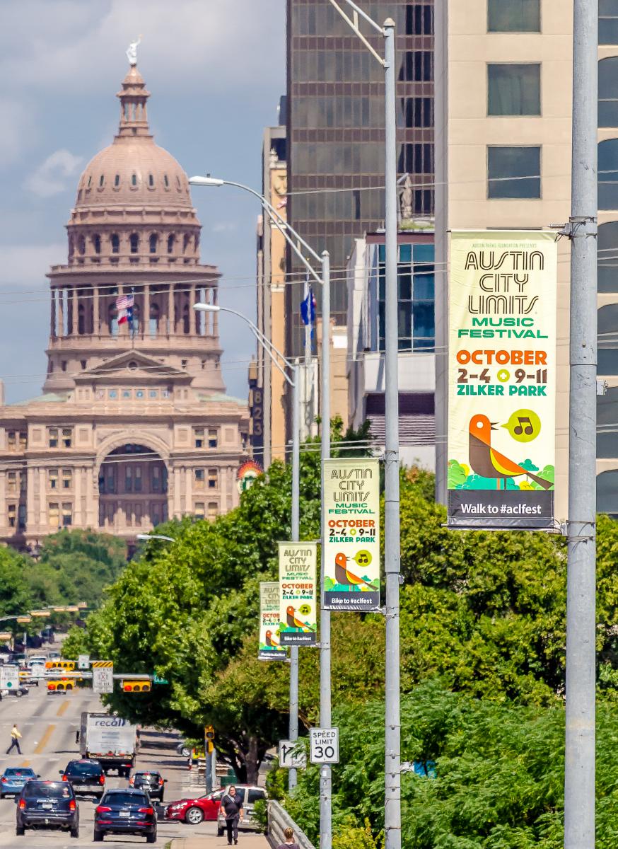 View of a line of street banners for Austin City Limits in front of the Capitol building.