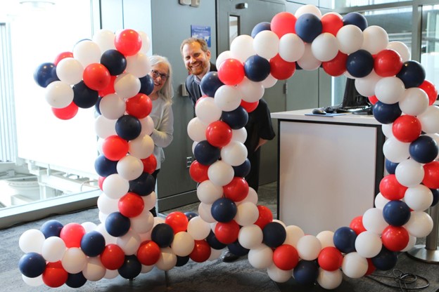 Two people smiling behind balloons that are the number 10.