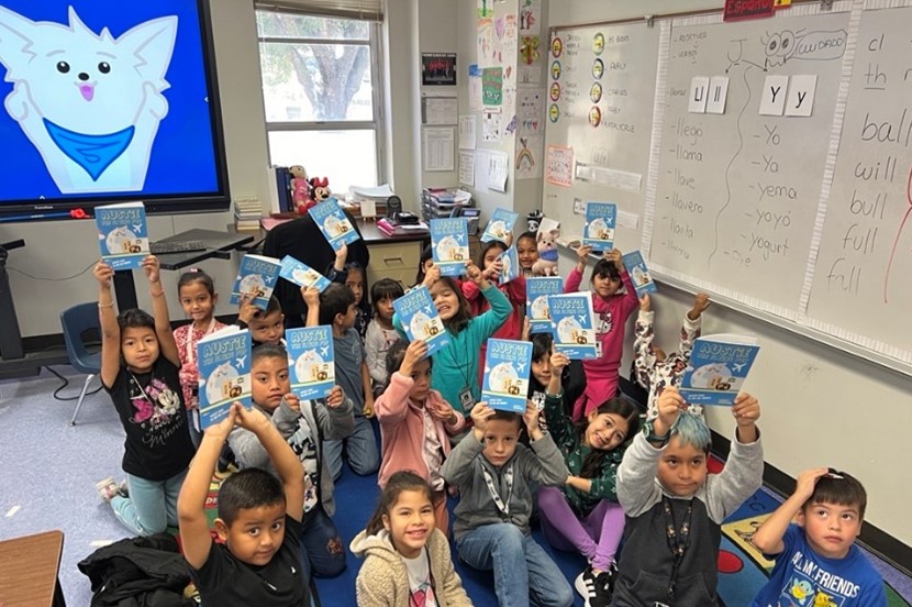 Kids holding up books. A dog in the background on a slideshow.