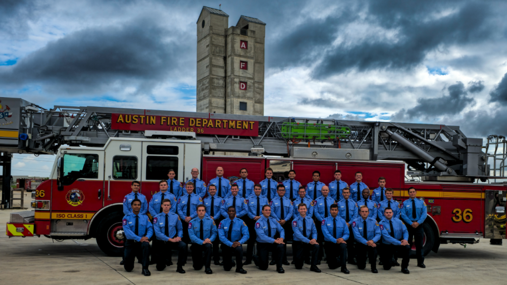 32 graduates of Austin Fire Department Class 137 lined up in three rows in front of Austin Fire Department Engine and Austin Fire Department Tower