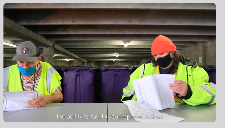 Photo of two men in face masks sitting at a table reading sheets of paper with a subtitle "the ability to talk to your representatives"