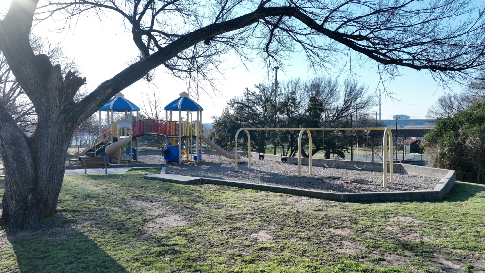 A long children's playscape is shown in the middle of the image with a large tree in the left side foreground.