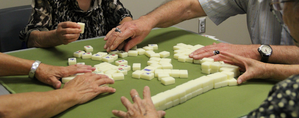 four seniors set up mahjong tiles on a green mat