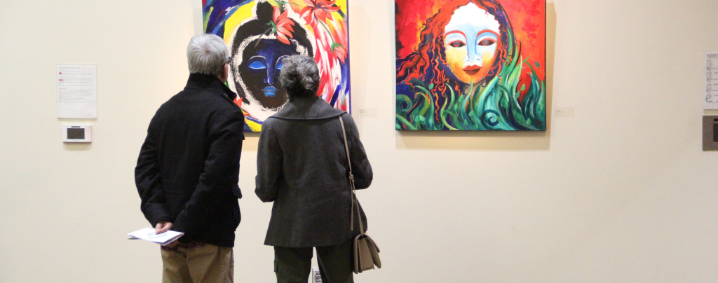 a man and woman look at a painting during a gallery opening