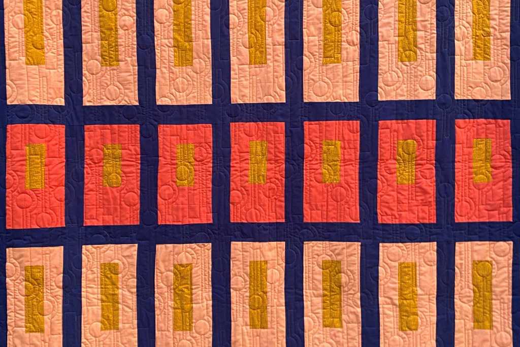 A close up image of a quilt with patchwork of colorful rectangles and quilting of circles and rectangles.