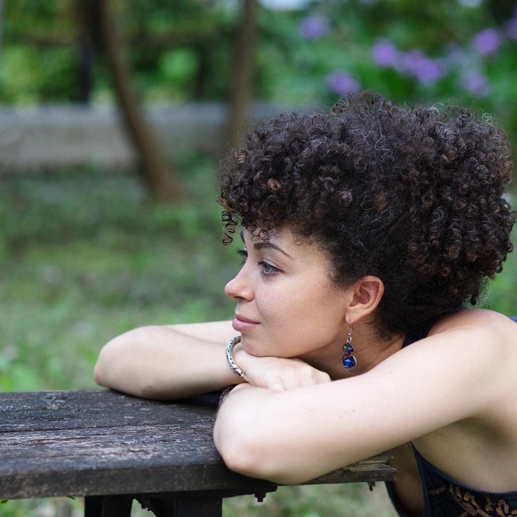 A photograph of artist Anna Gadzhikurbanova with her head resting on her folded arms