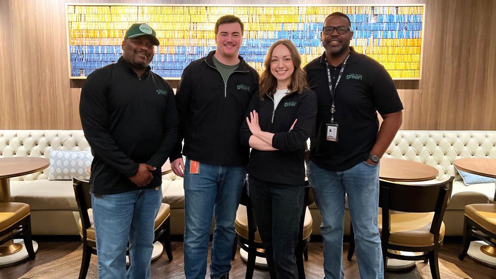 Four people stand in a row wearing black shirts that say, "keep the mood green."