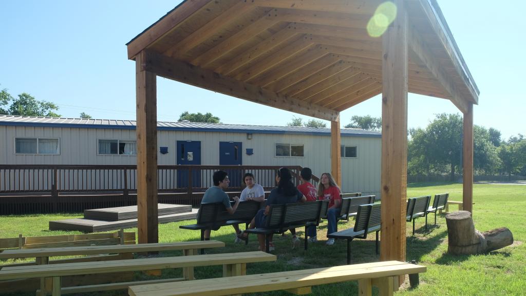 Sun shines in the outdoor classroom where Ms. Tapperson sits with students.