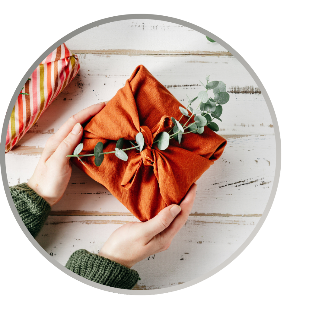 A close up on hands holding a gift wrapped in a cloth wrap with a floral decoration.