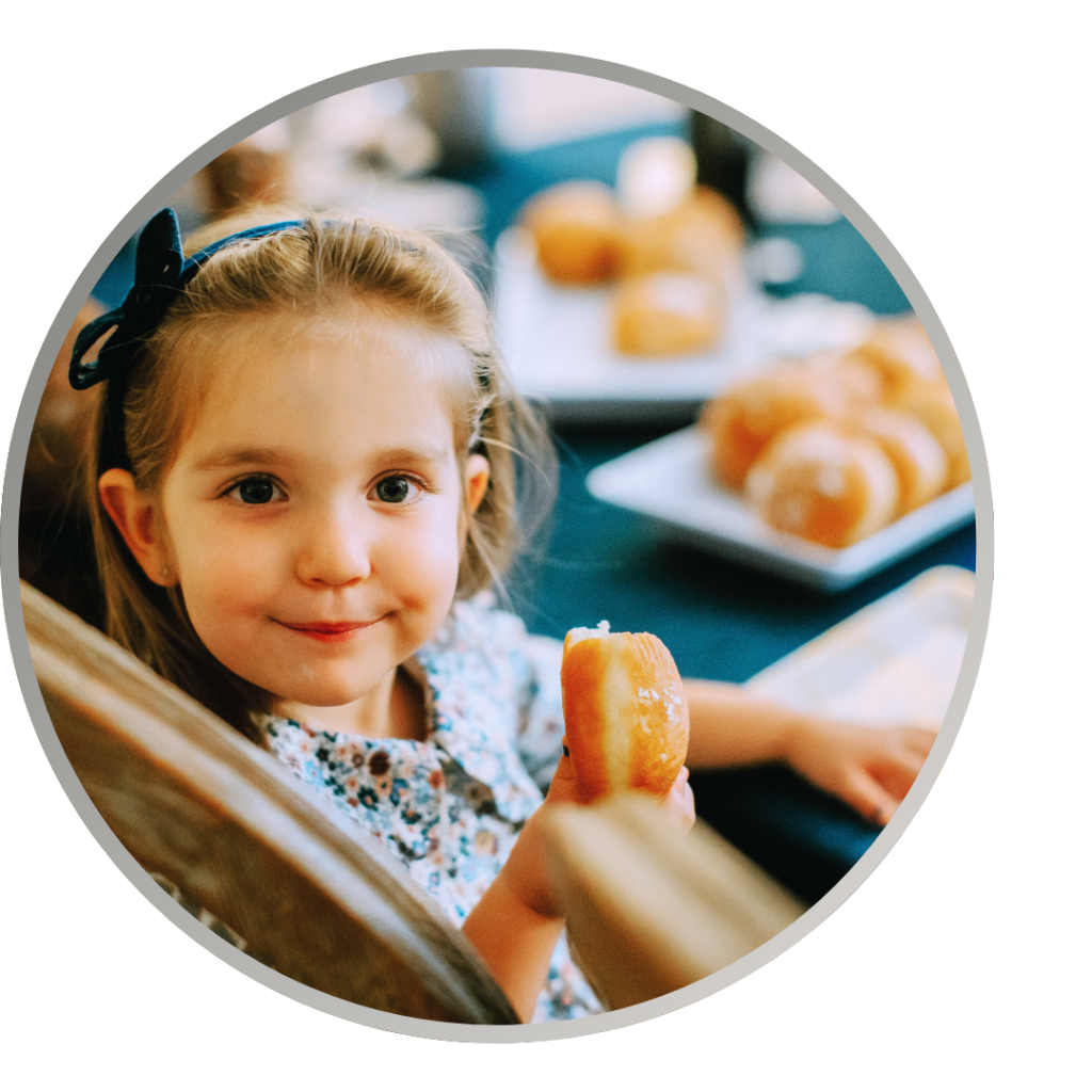 A young girl holds up a donut at a holiday table.