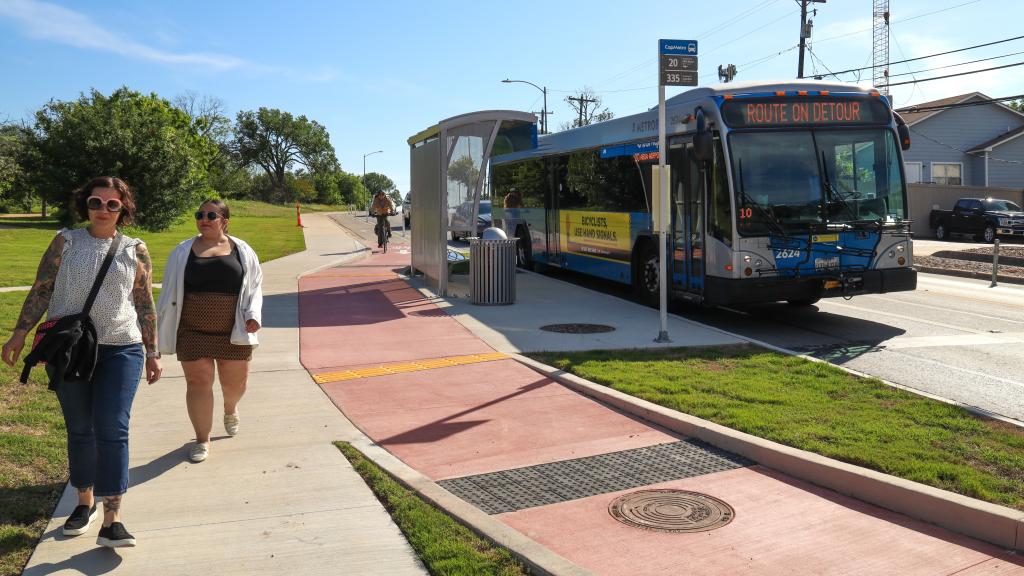 People walk along the sidewalk, away from a CapMetro bus at a stop.