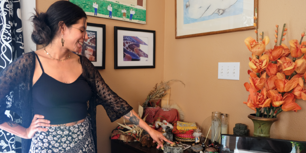 Chiara points to a small palo santo stick on a table with plants, candles, and other trinkets. 