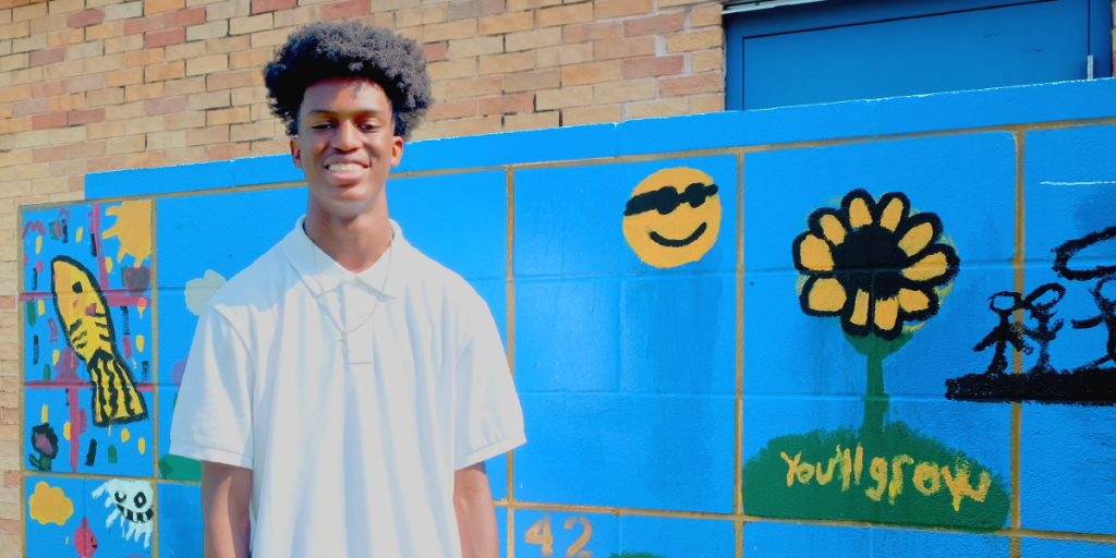 Elijah stands in front of a colorful mural that features a sunflower with the words, "You'll grow."