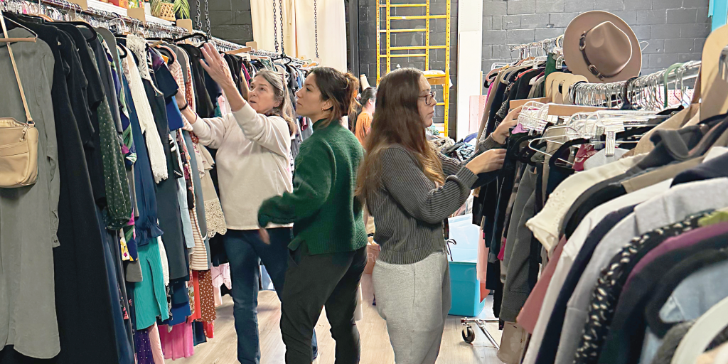 People stand between two racks of clothes placing items within them.