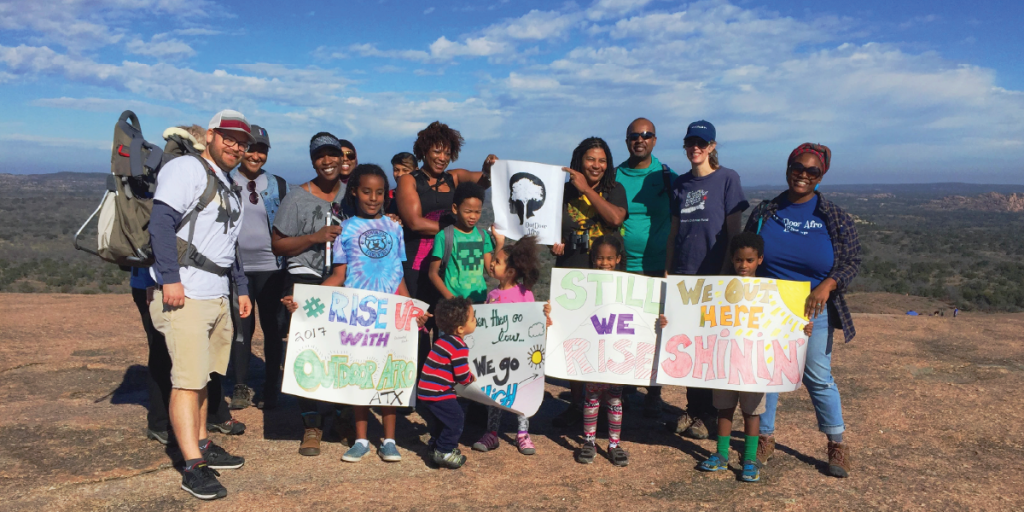 A group of families hold hand drawn signs on the top of Enchanted Rock.