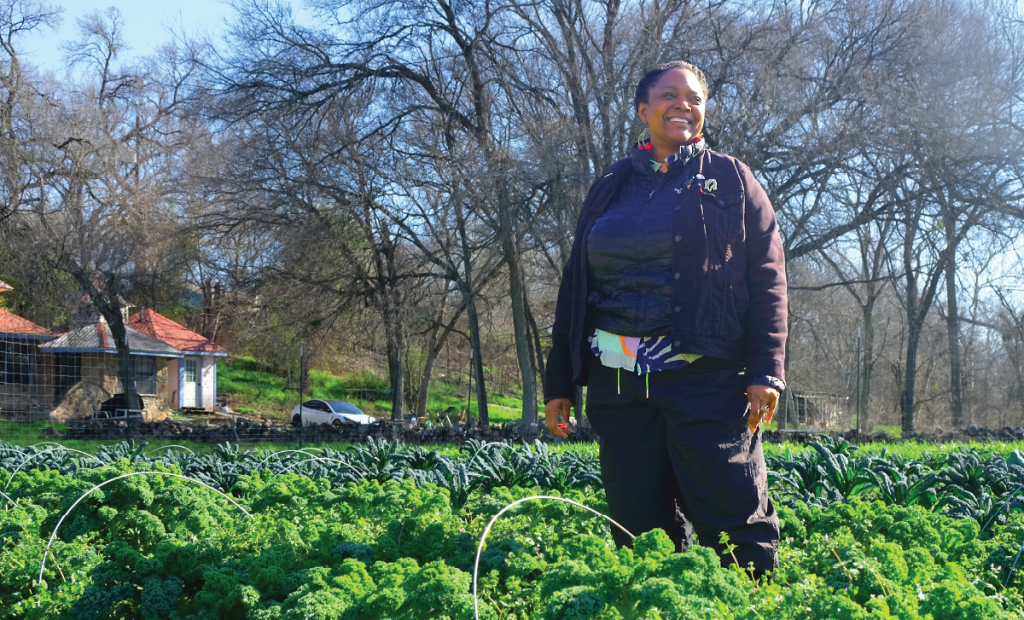 Starla stands in a field at Urban Roots' East Austin farm smiling and looking into the distance. 