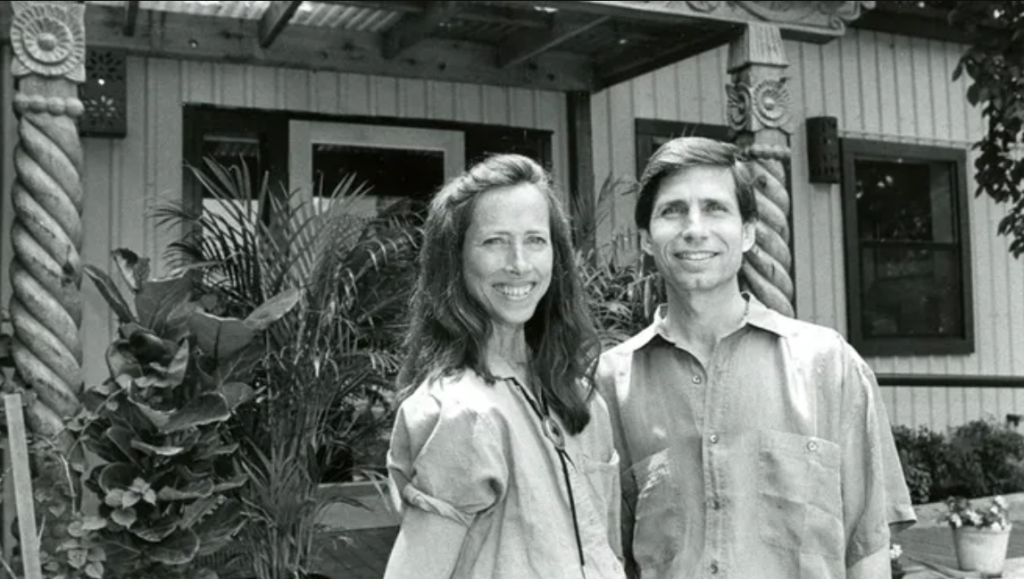 In a black and white photos, a young Maryann and Wayo stand at the entrance of Casa de Luz surrounded by plants.